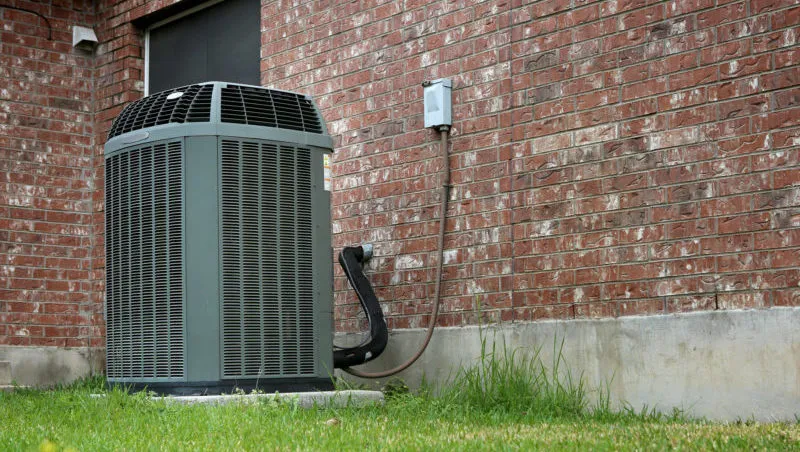 A heat pump displayed in front of a brick structure, representing efficient heating and cooling systems